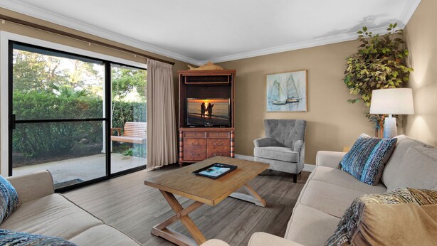 A spacious living room with a large sliding glass door leading to a balcony, a wooden coffee table, a grey armchair, and a beige sofa with patterned cushions. - 🌴 Winter Deal ❄️ Golf Cart-Heated Pool-FAB Reno- Seascape 22A🌊 (Miramar Beach)
