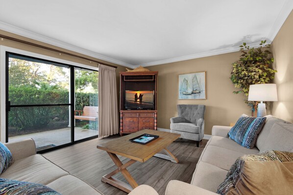 A spacious living room with a large sliding glass door leading to a balcony, a wooden coffee table, a grey armchair, and a beige sofa with patterned cushions. - 🌴 Winter Deal ❄️ Golf Cart-Heated Pool-FAB Reno- Seascape 22A🌊 (Miramar Beach)
