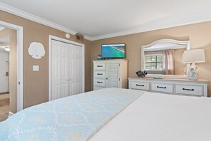 A bedroom with a bed, dresser, vanity, and a television on the wall.