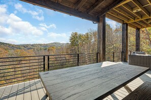 A wooden deck with a table and a wicker sofa, overlooking a forested hillside.
