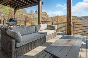 A covered outdoor deck with a wicker sofa, a table, and a grill.