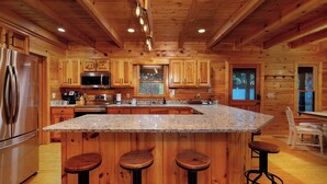 Una cocina amplia con armarios de madera, electrodomésticos de acero inoxidable y una isla de granito con taburetes de bar.