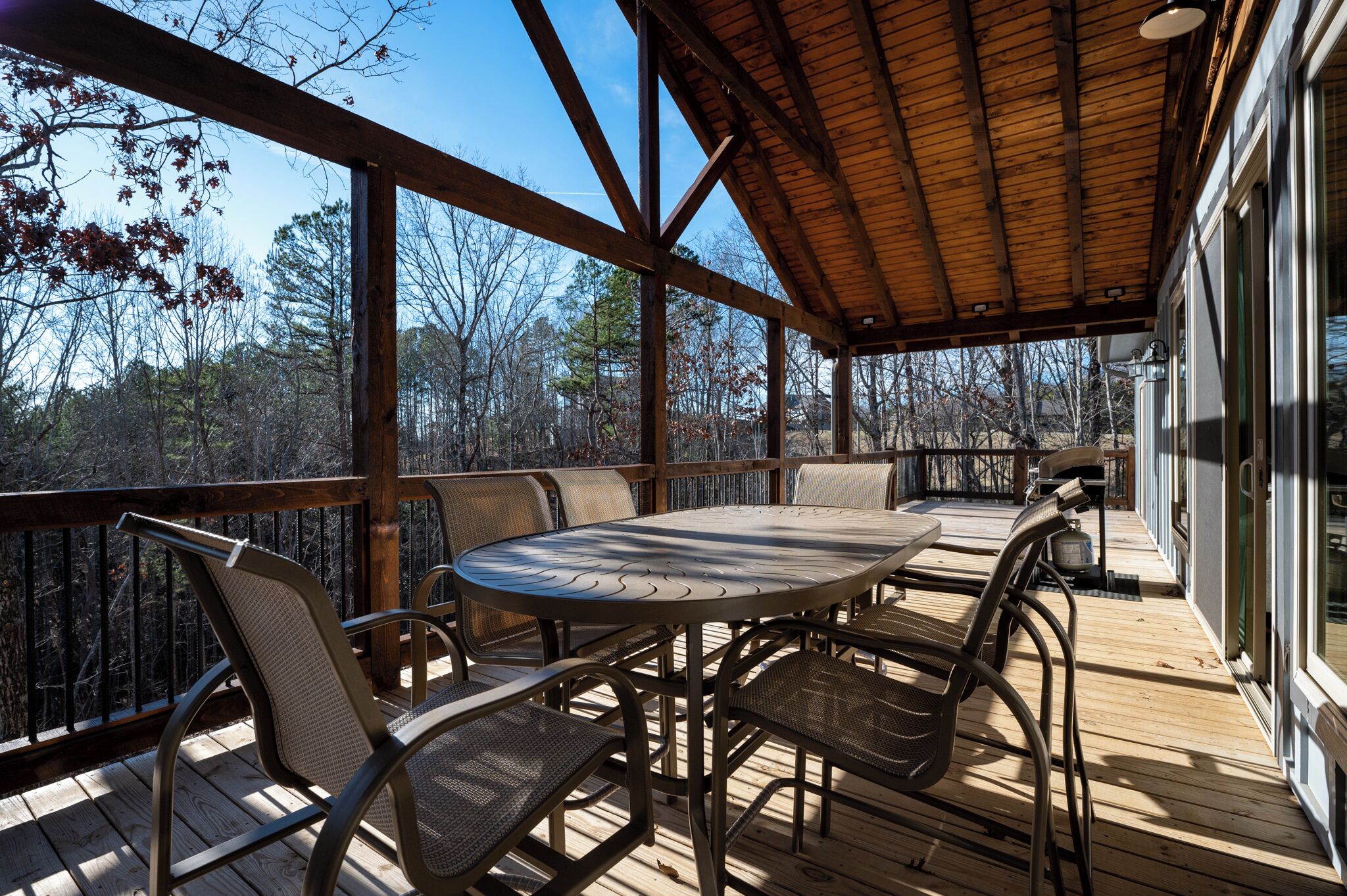 A covered outdoor deck with a round table and chairs, surrounded by a wooden railing.