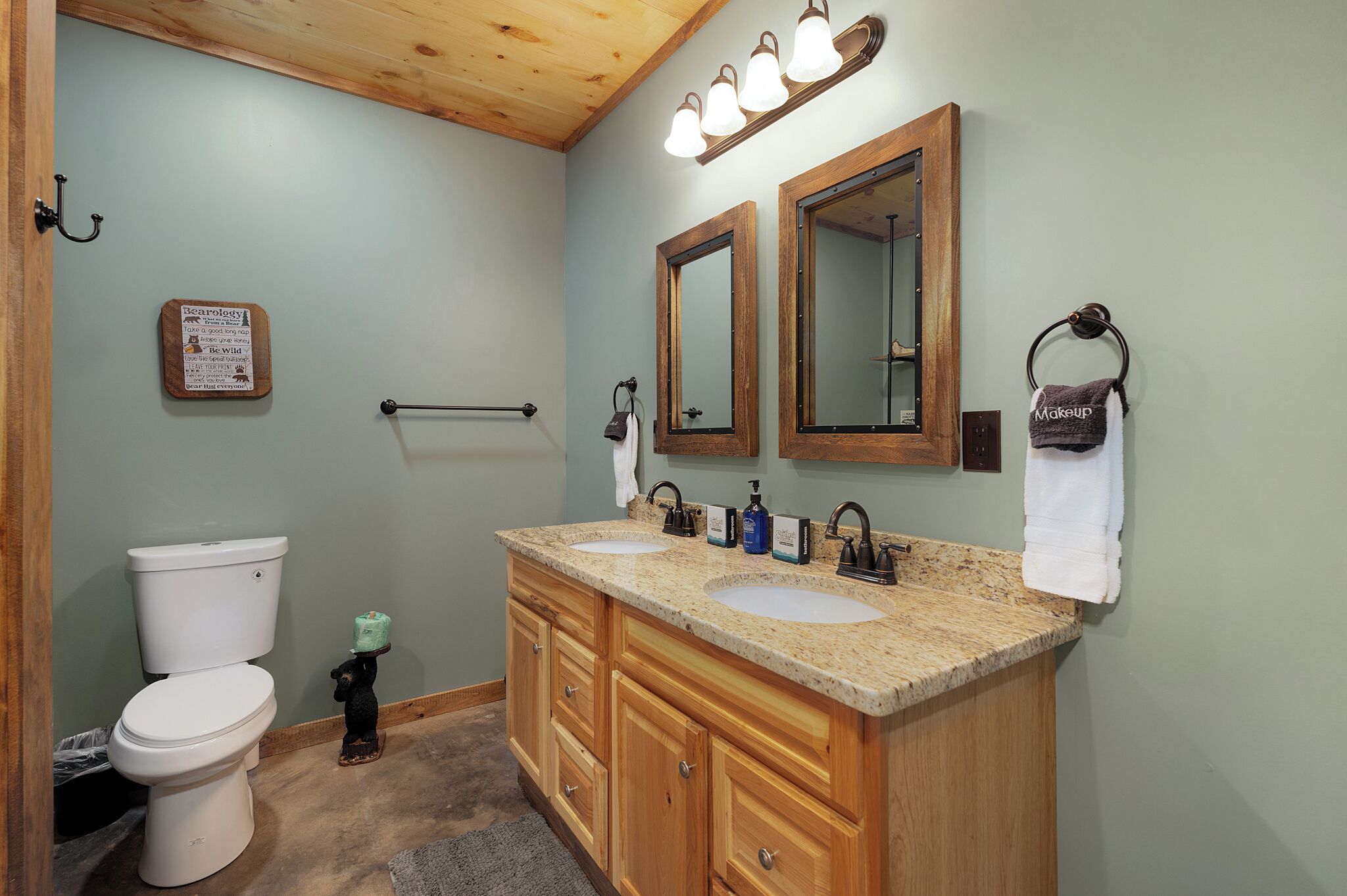 A bathroom with a wooden vanity, two sinks, a toilet, and a mirror.