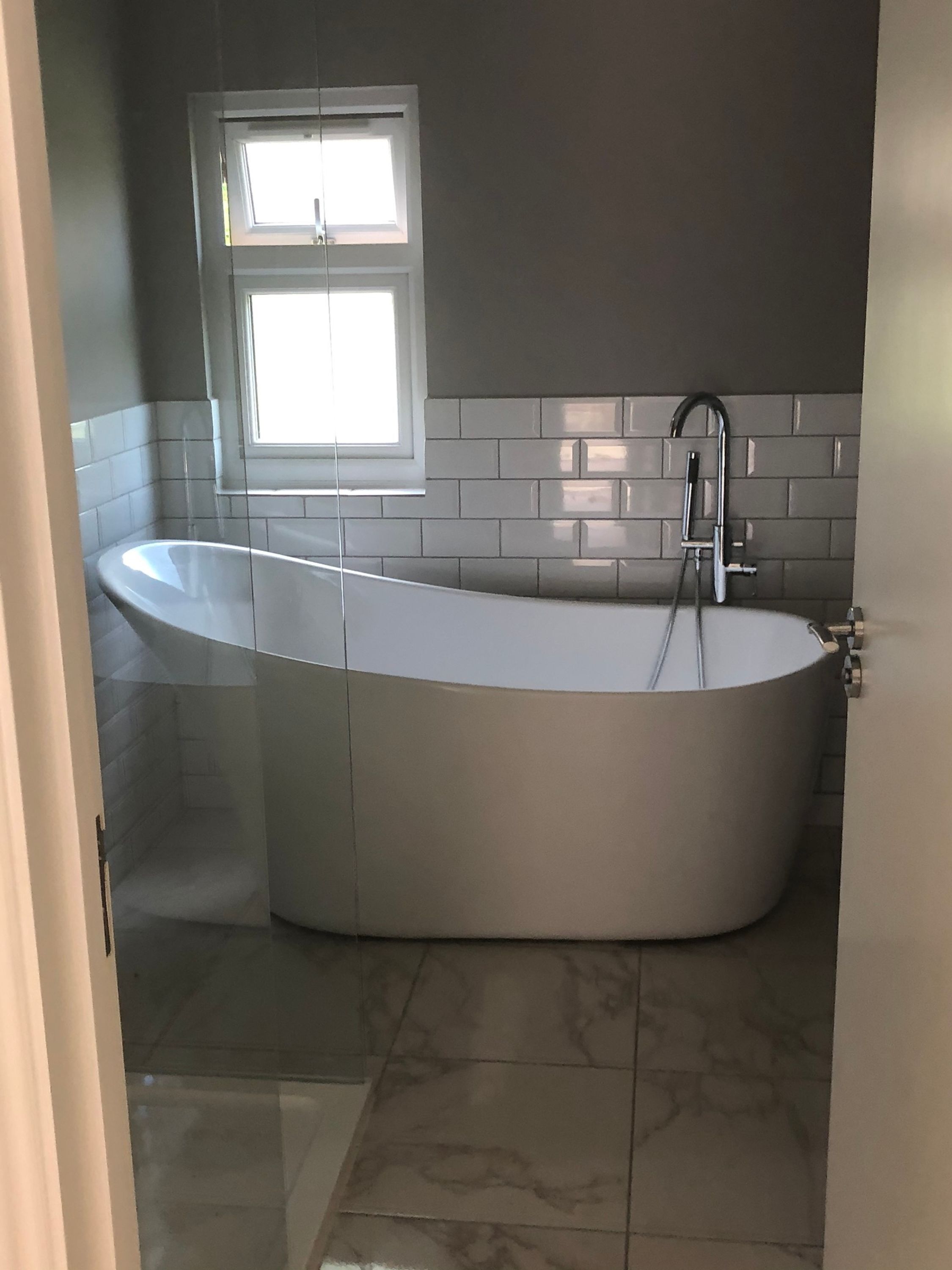 A modern bathroom with a freestanding bathtub, a window, and a tiled backsplash.