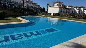Une piscine dont le fond est recouvert d’une mosaïque aux motifs bleus, entourée d’un mur de pierre et d’une clôture en bois.