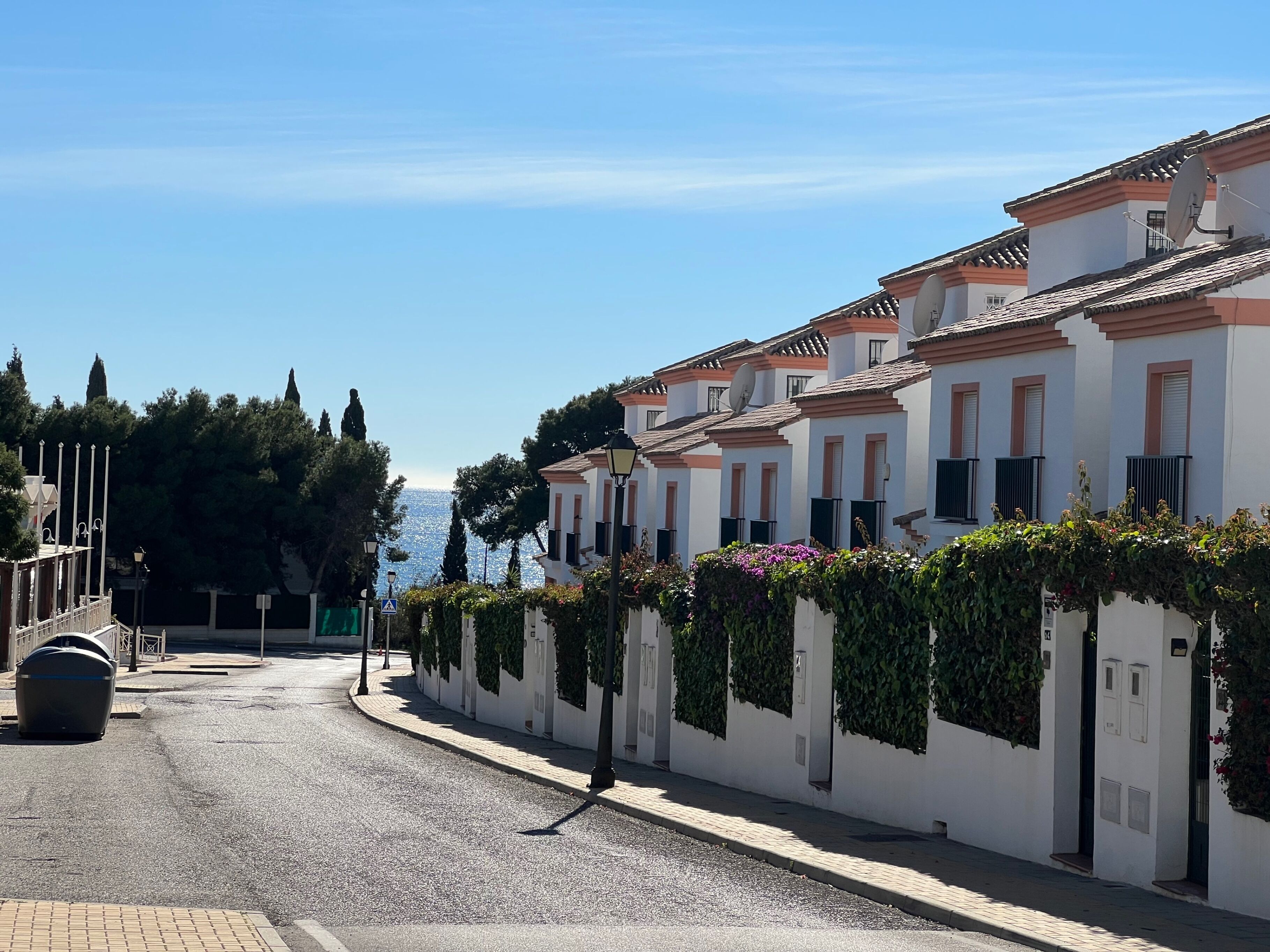 A row of white buildings with red-tiled roofs, a cobblestone street, and a clear blue sky.