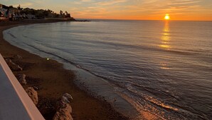 Une plage avec un coucher de soleil, une mer calme et des bâtiments en arrière-plan.