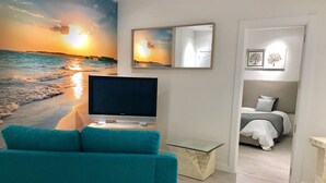 Un salon avec une grande télévision, un canapé de couleur turquoise et une fresque murale représentant une plage.