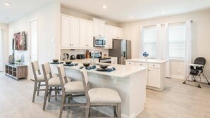 A spacious kitchen with white cabinetry, a central island with seating, and a dining area with chairs.