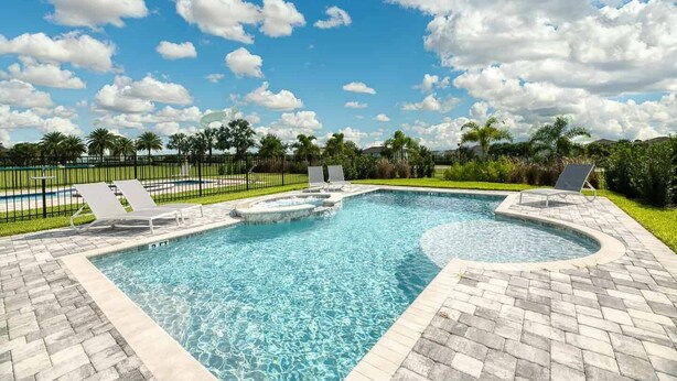 A swimming pool with lounge chairs and a paved deck, surrounded by greenery and palm trees.