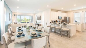 A modern kitchen with white cabinets, a central island, and a dining area with a glass table and chairs.