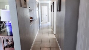 A hallway with a tiled floor, a door at the end, and a table with a lamp on the left. - TERRA NOVA Spacious 4-bedroom house in Phoenix AZ, 7 minutes from Downtown. (Phoenix)