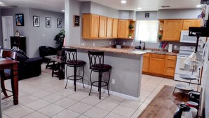 A modern kitchen with wooden cabinets, a central island with stools, a dining area with a table and chairs, and a living room with a sofa and a coffee table. - TERRA NOVA Spacious 4-bedroom house in Phoenix AZ, 7 minutes from Downtown. (Phoenix)
