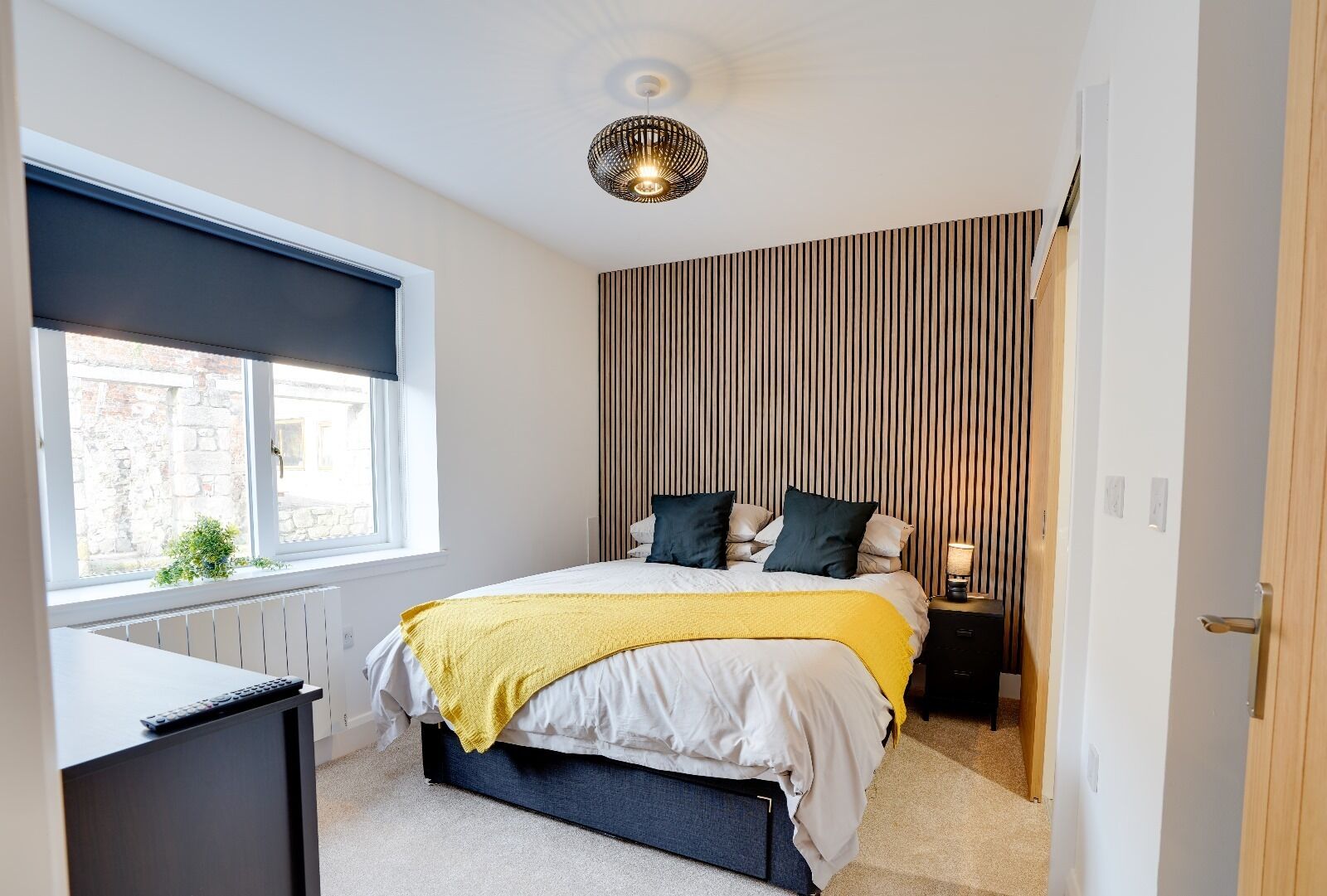 Ein Schlafzimmer mit Bett, Nachttisch, Lampe, Fenster und Heizkörper.