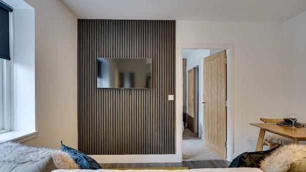 Un salon moderne doté d’un téléviseur à écran plat fixé au mur, d’un canapé avec des coussins moelleux et d’un coin repas comprenant une table et des chaises.