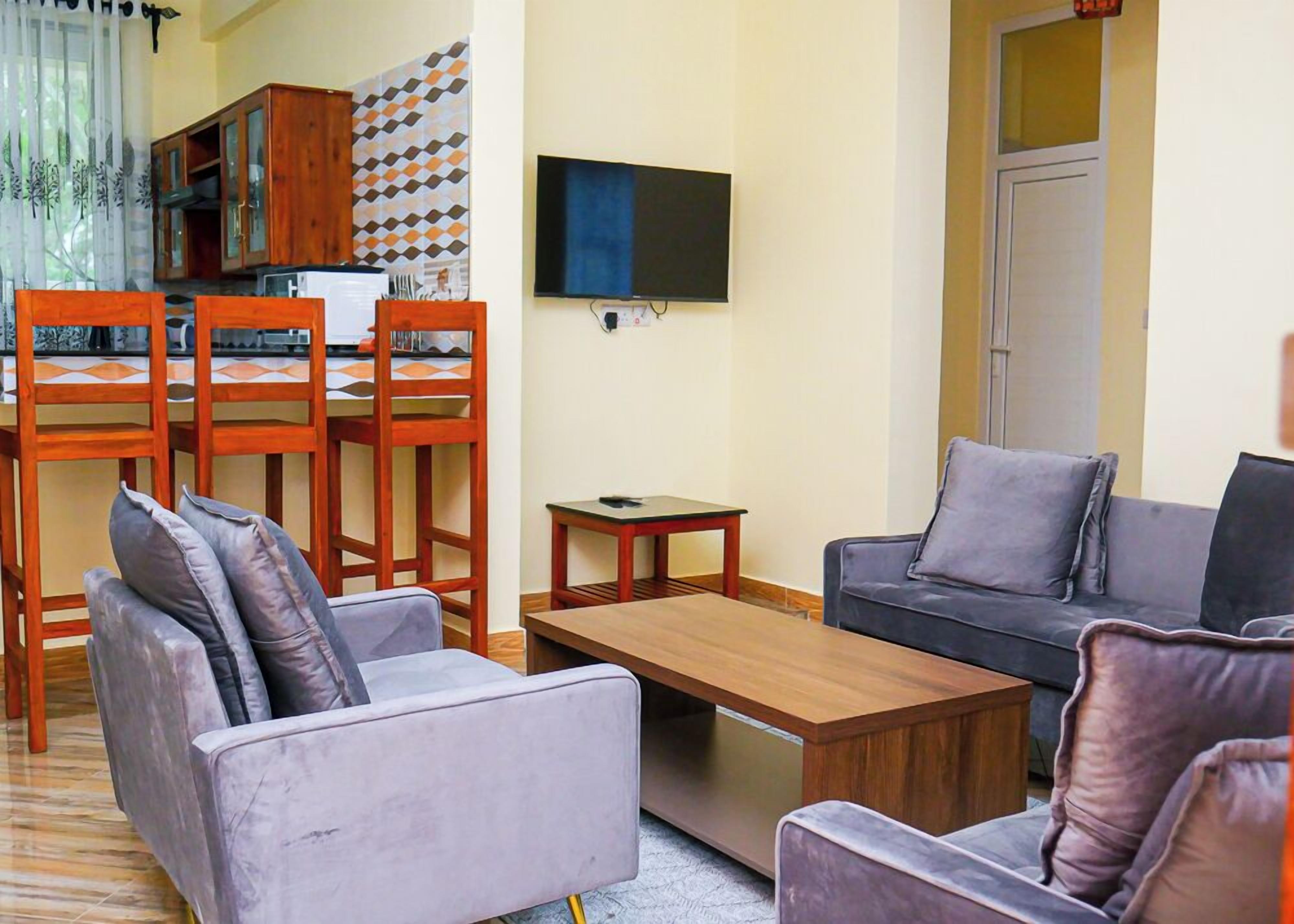 A living room with a sofa, armchairs, a coffee table, a TV, and a dining area with chairs and a table.