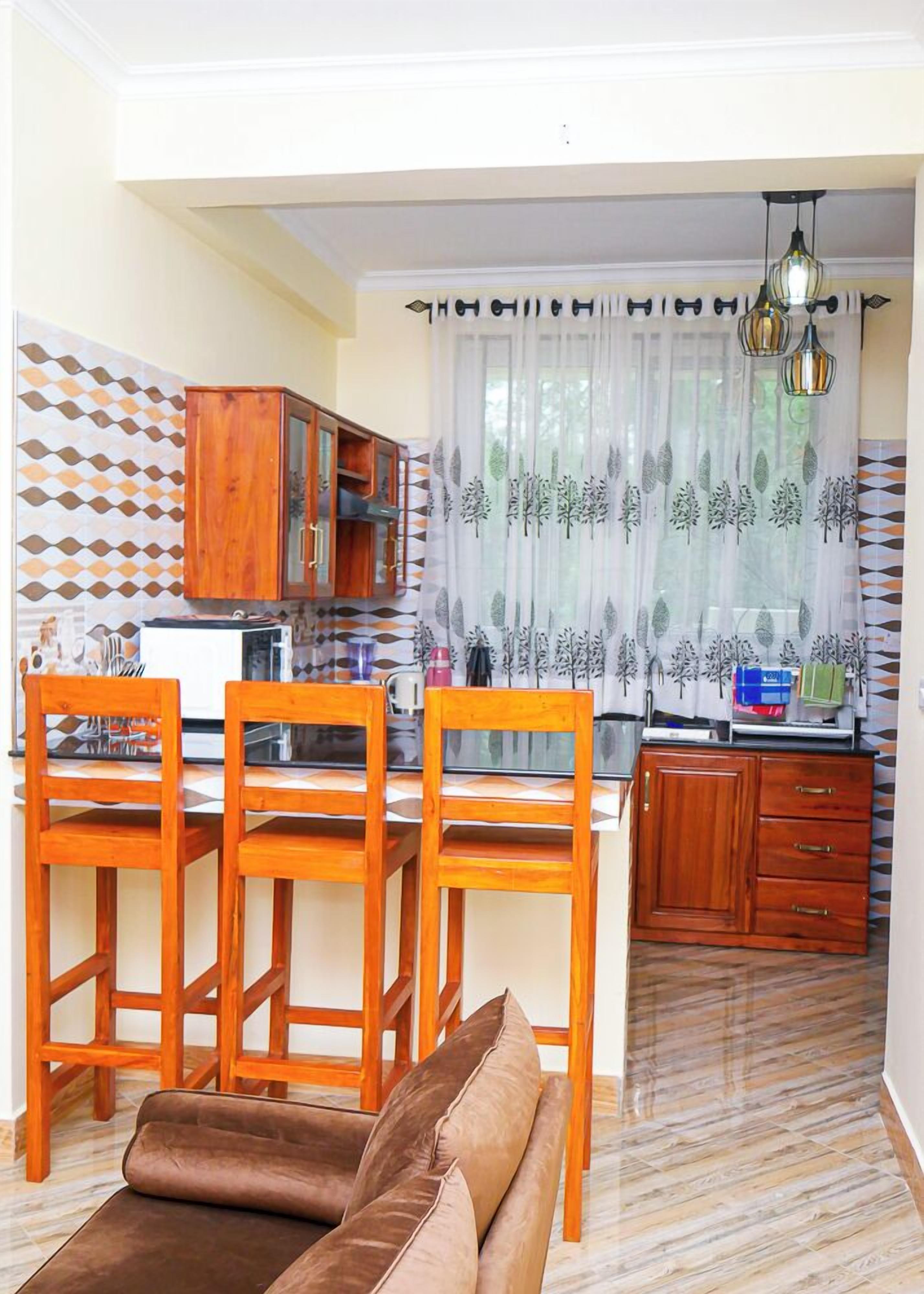 A compact kitchen with wooden cabinets, a dining area with a brown sofa, and a patterned wall.
