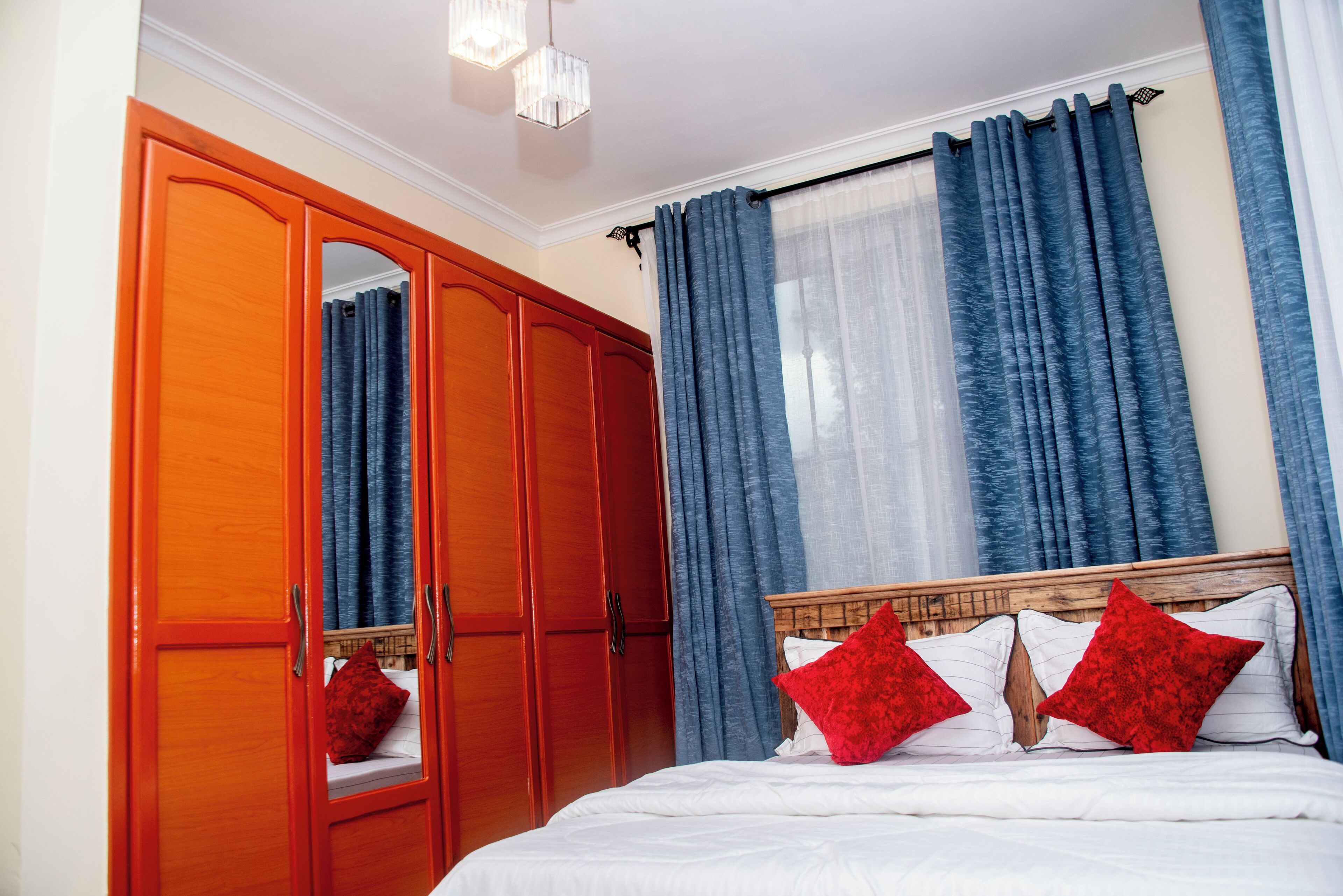 Une chambre avec une armoire en bois, un lit avec une literie blanche et des oreillers rouges, et des rideaux bleus.