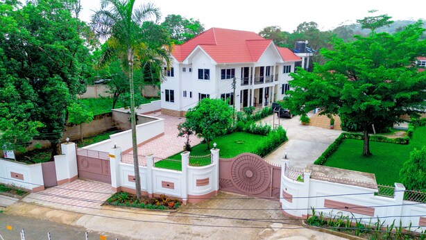 A two-story white house with a red roof, surrounded by lush greenery and a well-maintained garden. - VvEK BED AND BREAKFAST APARTMENT (Arusha)