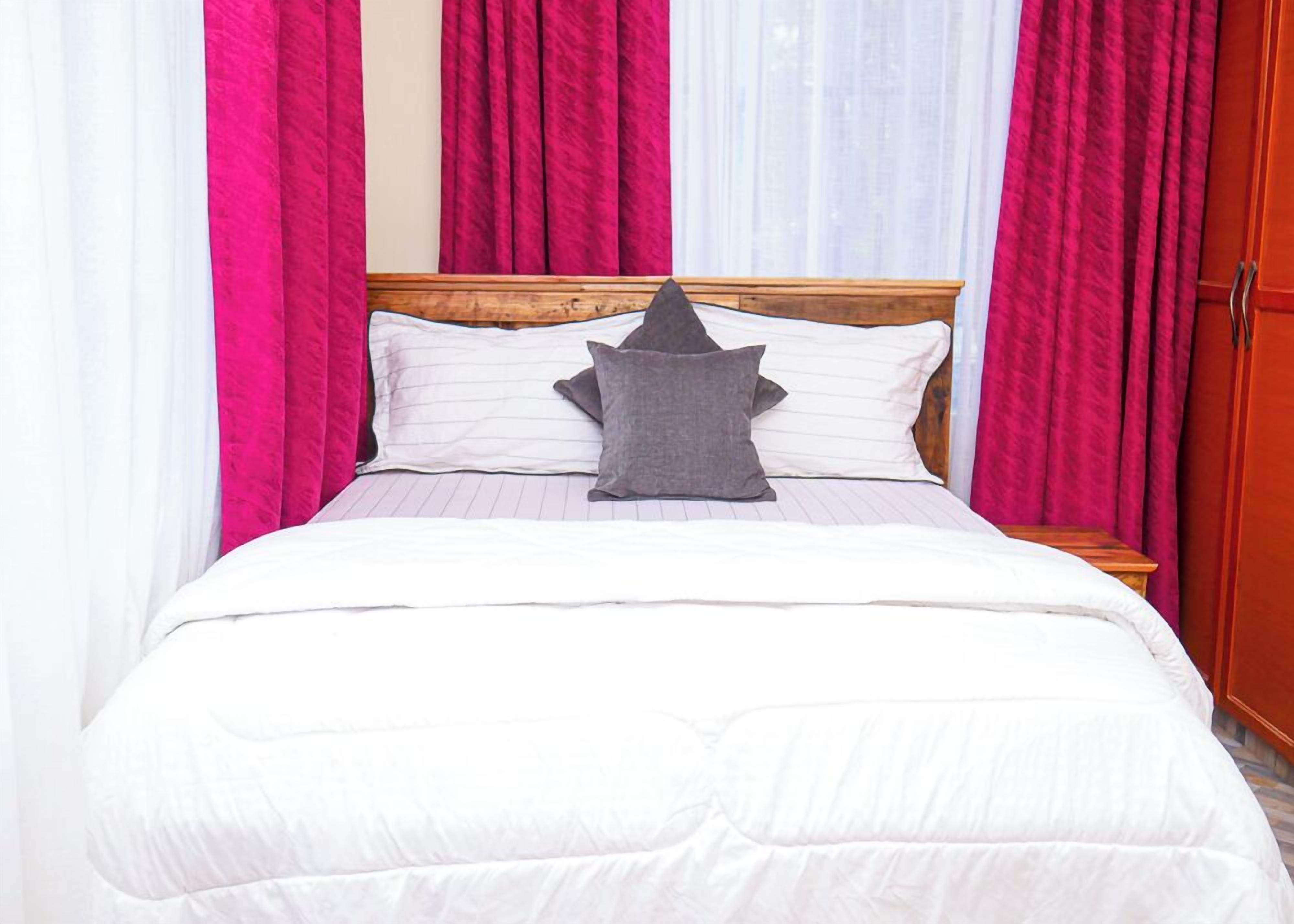 A bed with a white comforter and pillows, a wooden headboard, and pink curtains.