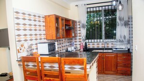 A kitchen with wooden cabinets, a microwave, and a dining area with chairs. - VvEK BED AND BREAKFAST APARTMENT (Arusha)