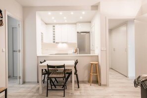 A modern kitchen with white cabinets, a stainless steel refrigerator, and a dining area with a table and chairs. - Letassi - Edificio Saburedo (Baqueira)