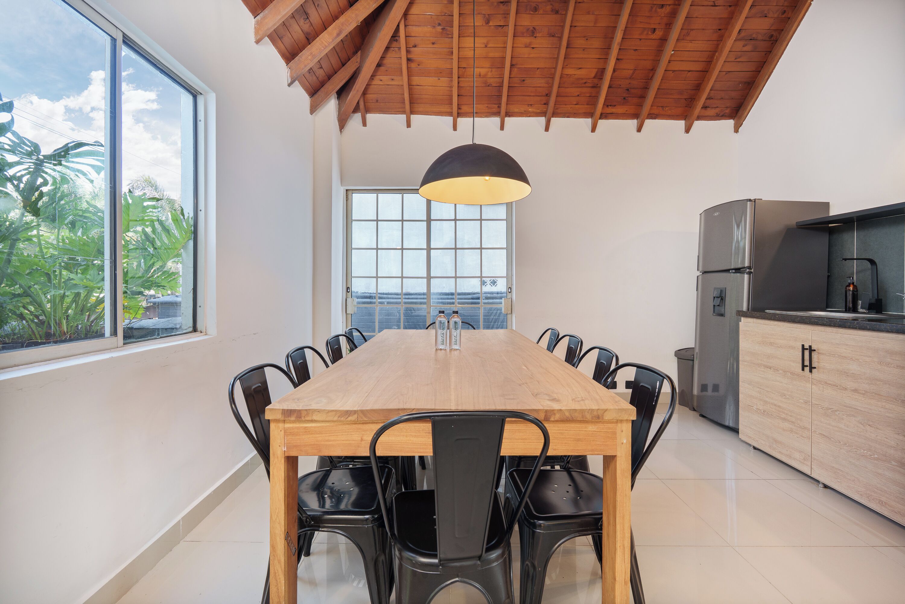 A modern kitchen with a wooden dining table, black chairs, a large window, and a view of the outdoors.