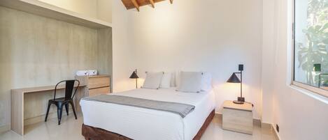 A bedroom with a wooden bed frame, a desk, a chair, and a nightstand with a lamp.