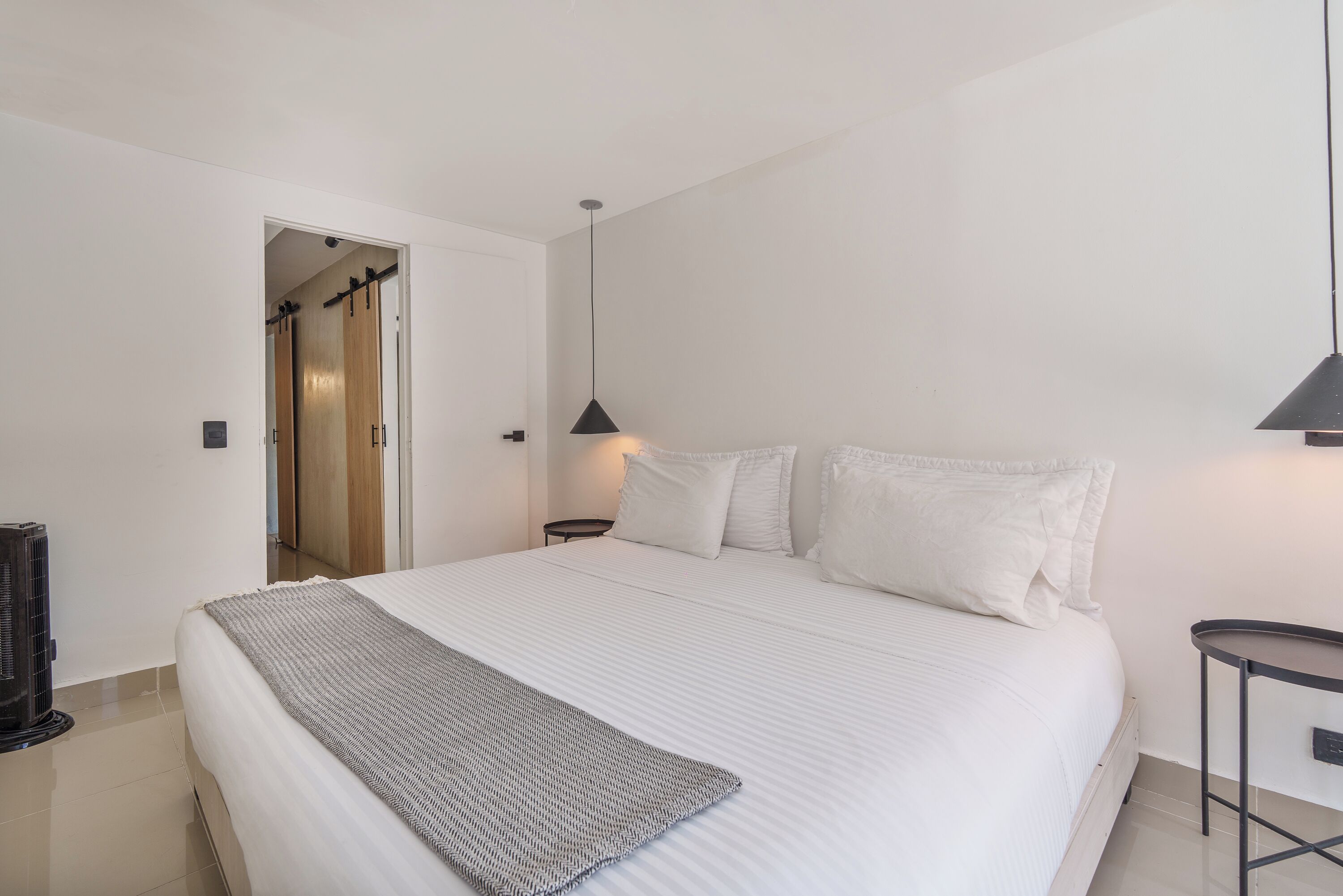 Une chambre à coucher comprenant un lit, des tables de chevet, une lampe et une porte donnant sur une autre pièce.