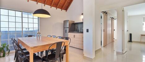 Une cuisine spacieuse avec un plafond en bois, un coin repas avec une table et des chaises en bois, et une vue dégagée grâce à de grandes fenêtres.