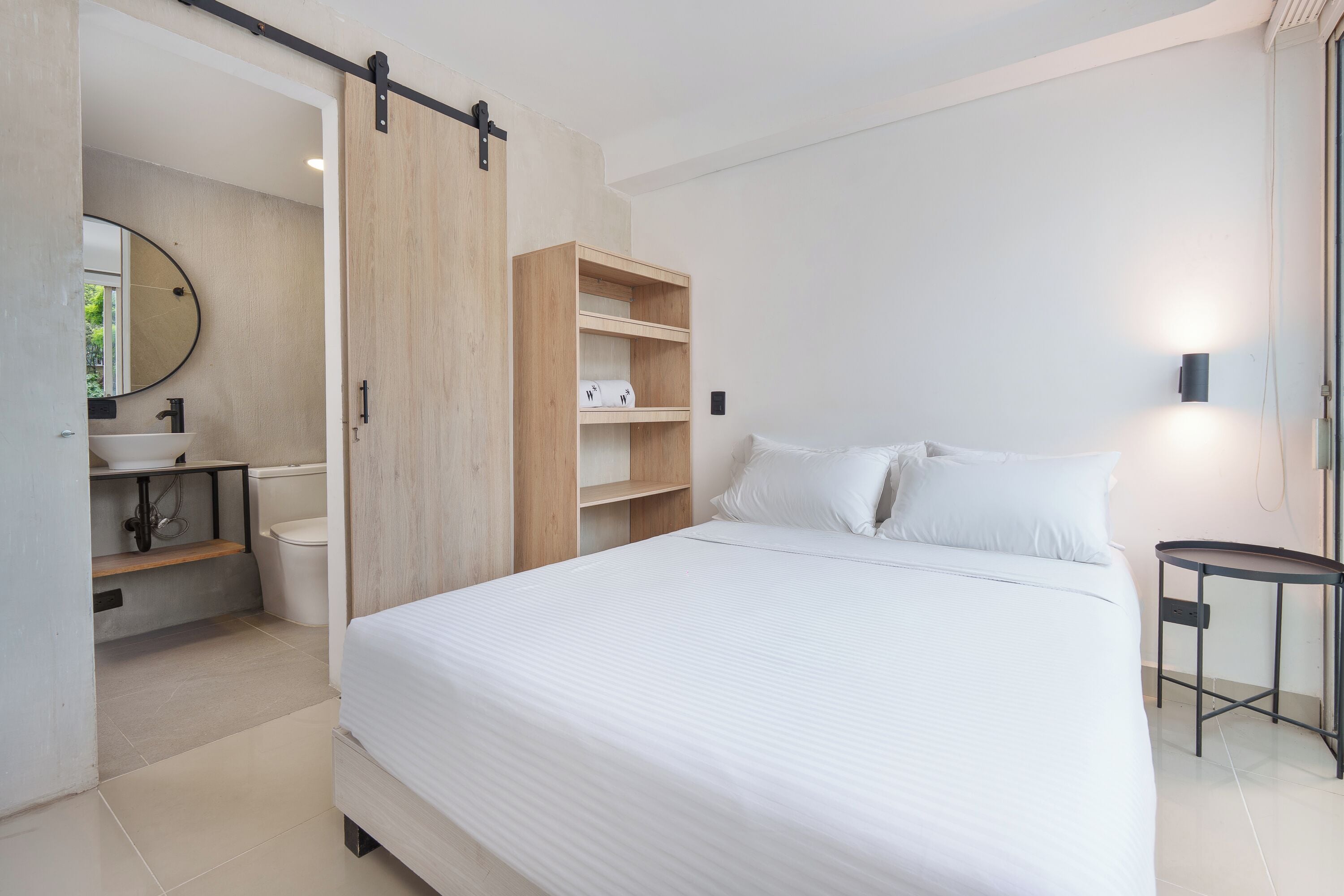 A modern bedroom with a large bed, a wooden wardrobe, a bedside table, and a bathroom with a toilet and sink.