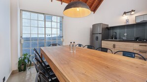 A modern kitchen with a wooden dining table, chairs, a large window, and a ceiling with exposed beams. - Hotel Santa Ana (Medellín)