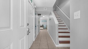 A hallway with a white door, a sign indicating a toilet, and a staircase with wooden steps. - Southbay by the Gulf #32 - Destination Destin (Destin)