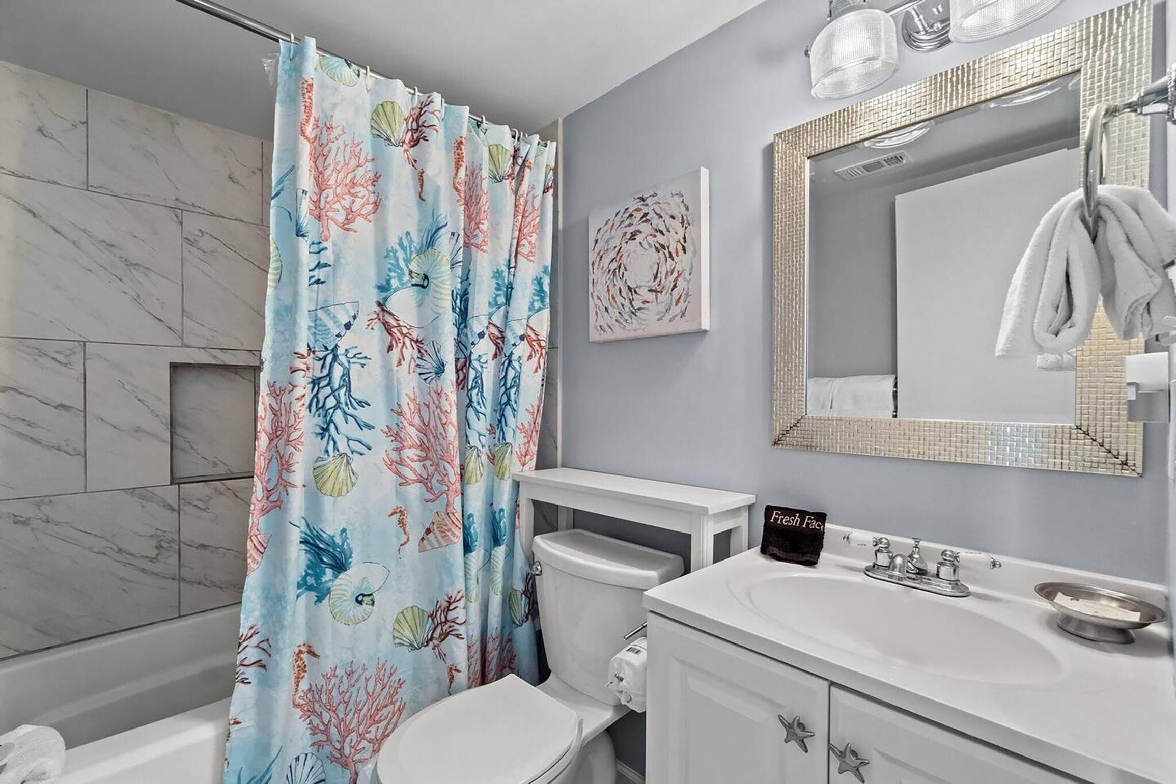Un baño con inodoro, lavamanos y cortina de ducha con estampado de coral y conchas.