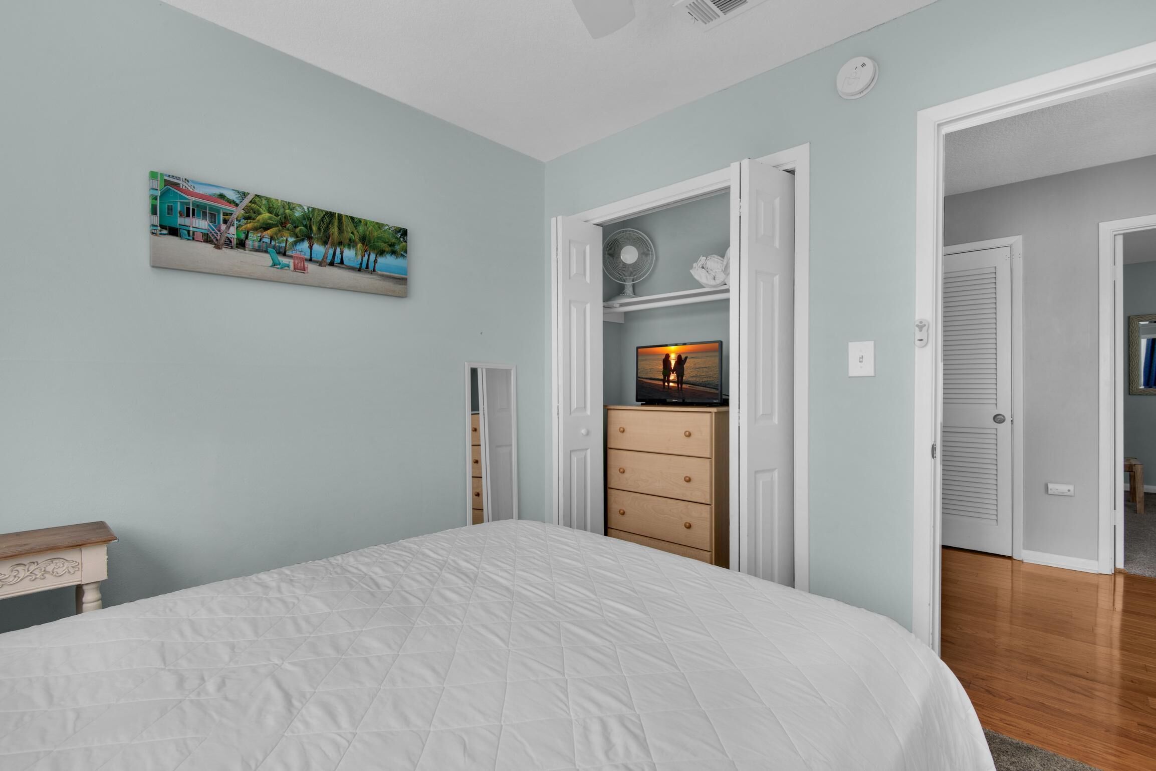 Un dormitorio con cama, cómoda, un cuadro y una puerta que da a otra habitación.