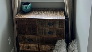 A window with a view of a lake and autumn trees, a rustic wooden bench with a ceramic pot, and a fluffy white pillow. - The Stillwater Suite, named after the serene stillness of its surroundings and the moments where the lake is as still as glass. (Jasper)