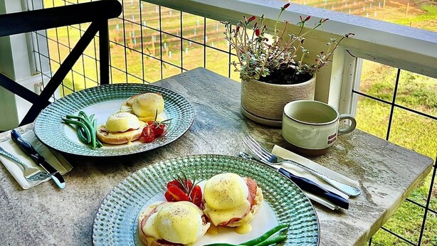 A balcony with a table set for breakfast, featuring eggs benedict and green beans, overlooking a lush green landscape. - The Stillwater Suite, named after the serene stillness of its surroundings and the moments where the lake is as still as glass. (Jasper)