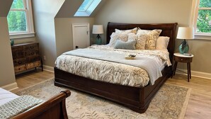 A bedroom with a large bed, a skylight, a dresser, and two bedside lamps. - The Stillwater Suite, named after the serene stillness of its surroundings and the moments where the lake is as still as glass. (Jasper)