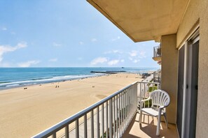 Un balcón con vista a una playa y al océano, una silla blanca y la fachada de un edificio.
