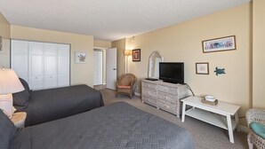 A hotel room with two beds, a dresser, a television, and a chair.