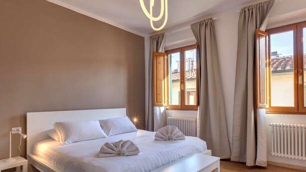 A modern bedroom with a large bed, bedside tables, a bench, and a view of the outside. - Mamo Florence - Sacha Apartment (Florence)