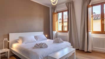 Quarto moderno com uma cama grande, mesas de cabeceira, um banco e vista para o exterior.