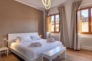 Une chambre à coucher moderne avec un grand lit, des tables de chevet, un banc et une vue sur l’extérieur.