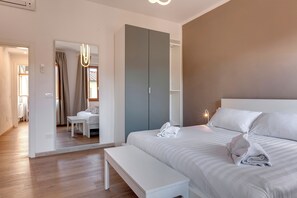 A modern hotel room with a large bed, a bench, a wardrobe, and a mirror. - Mamo Florence - Sacha Apartment (Florence)