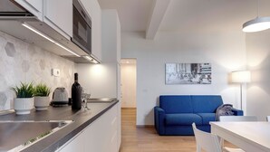 A modern kitchen with a built-in island, white cabinetry, and a blue sofa in the living area. - Mamo Florence - Sacha Apartment (Florence)