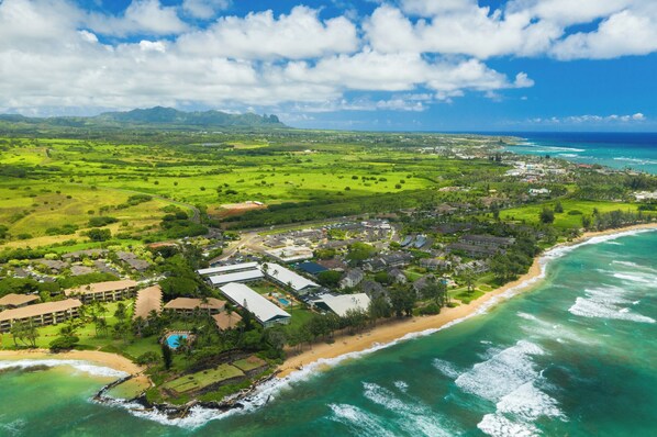 An aerial view of a coastal resort with beachfront properties, a golf course, and a large hotel complex.