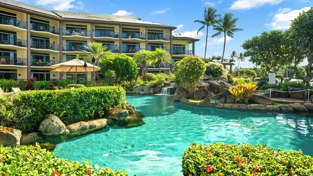 A hotel with multiple balconies, a swimming pool, and lush landscaping. - Summer Deal Oceanfront Poipu Condo with Heated Pool and Lanai (Koloa)