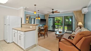A modern kitchen with white cabinets, a refrigerator, and a dining area with a table and chairs. - Summer Deal Oceanfront Poipu Condo with Heated Pool and Lanai (Koloa)