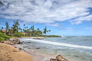 A beach with clear skies, palm trees, and a rocky shoreline. - Summer Deal Kapaa Cottage with Garden Steps from the Beach (KAPAA)